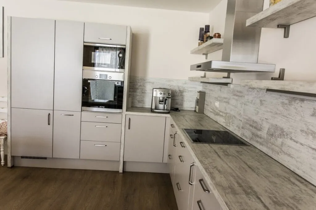 Modern kitchen with grey cabinets, built-in oven and microwave, induction cooktop, stainless steel hood, and coffee maker.