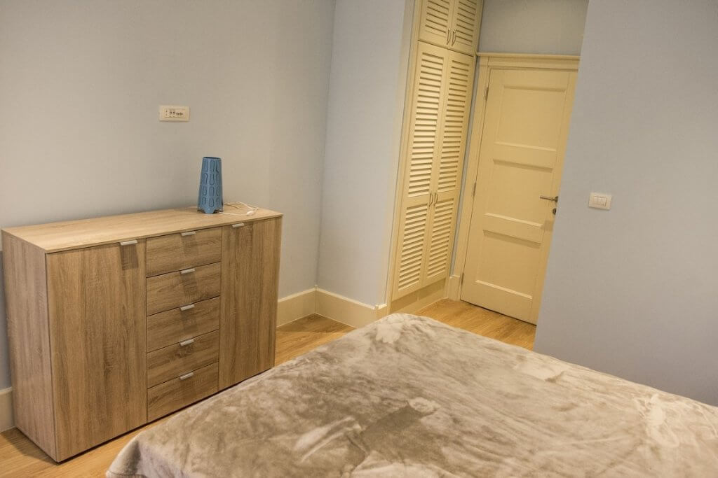 Bedroom with a wooden dresser and built-in wardrobe in a villa, Stoliv, Montenegro. Bright interior with laminate flooring.