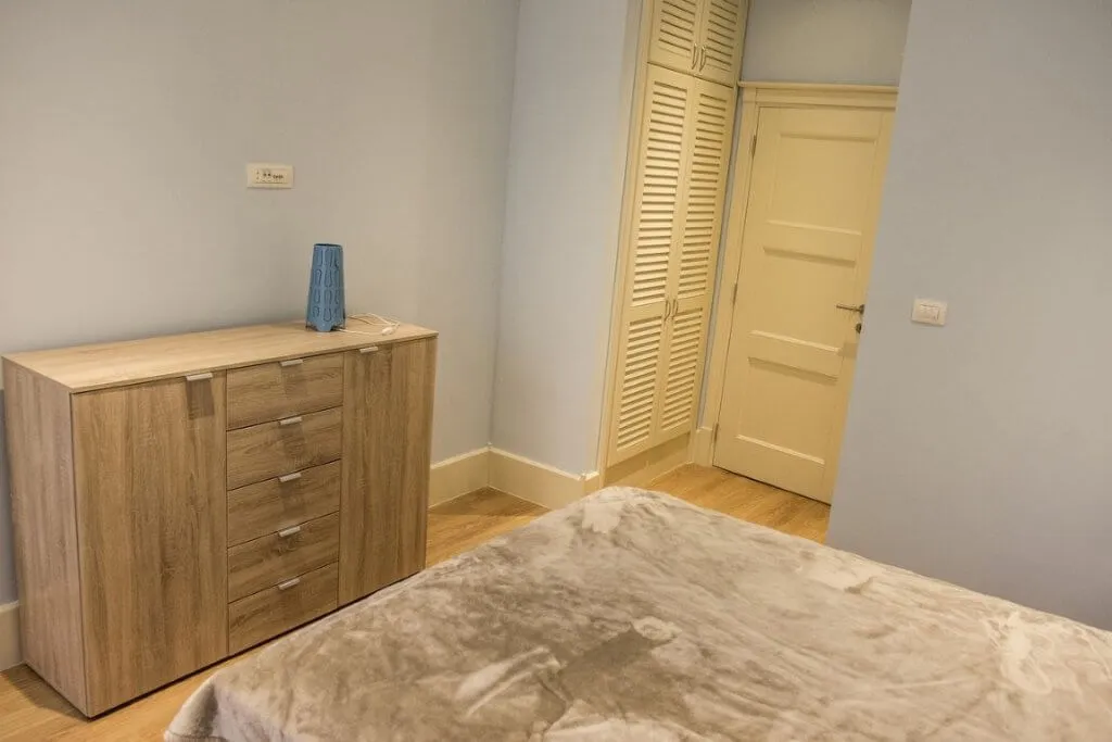 Bedroom featuring a wooden dresser, part of a bed with a grey cover, and a louvered closet door.