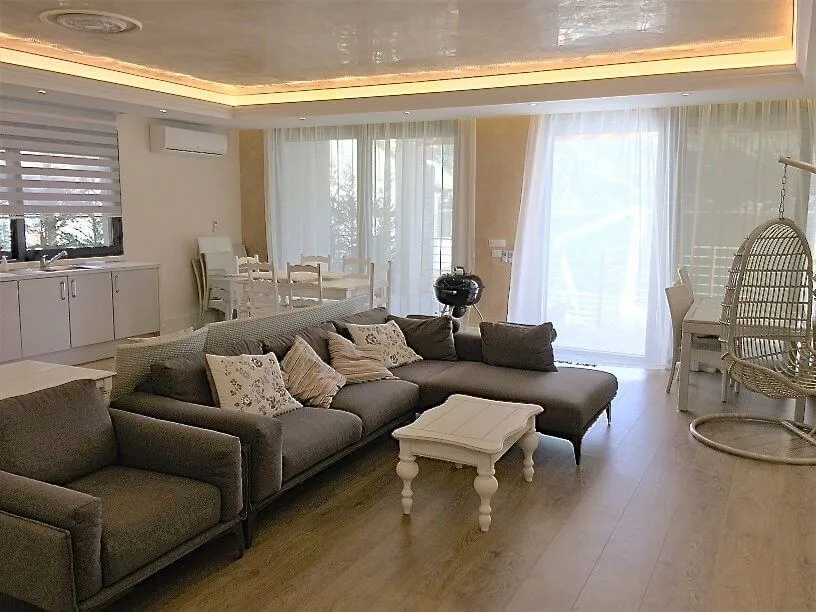 Living room featuring a large grey sectional sofa, white coffee table, and dining area near kitchen.