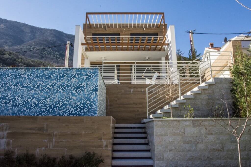 Modern villa in Stoliv, Montenegro: facade with a terrace, swimming pool, and stone finish against a mountain backdrop.