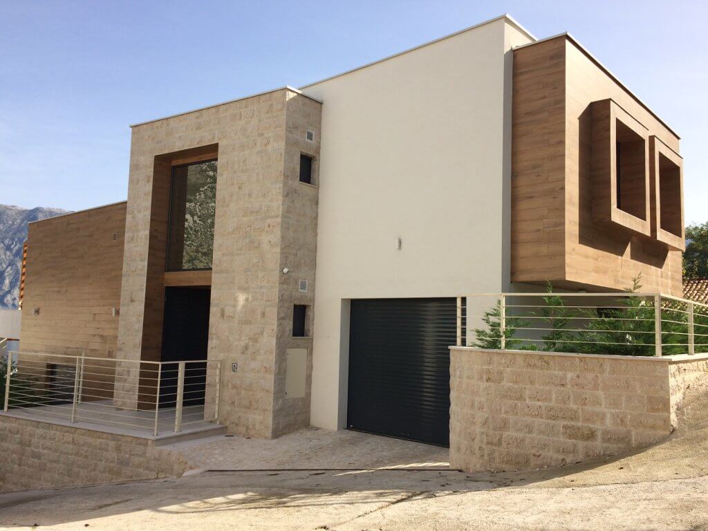 Modern villa in Stoliv, Montenegro: facade with stone and wood finishes, garage, and panoramic glazing.
