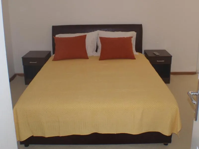 Bed with yellow cover and orange pillows, two dark nightstands against a plain white wall.