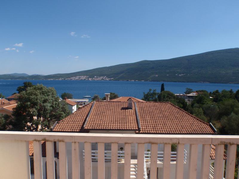 View from the balcony of a house in Baošići, Montenegro: a panorama of the sea, mountains, and tiled roofs on a sunny day.
