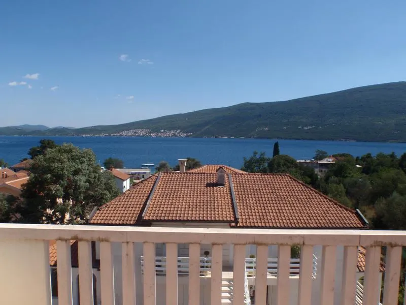View from a balcony showing a tiled roof, blue sea, and green mountains.