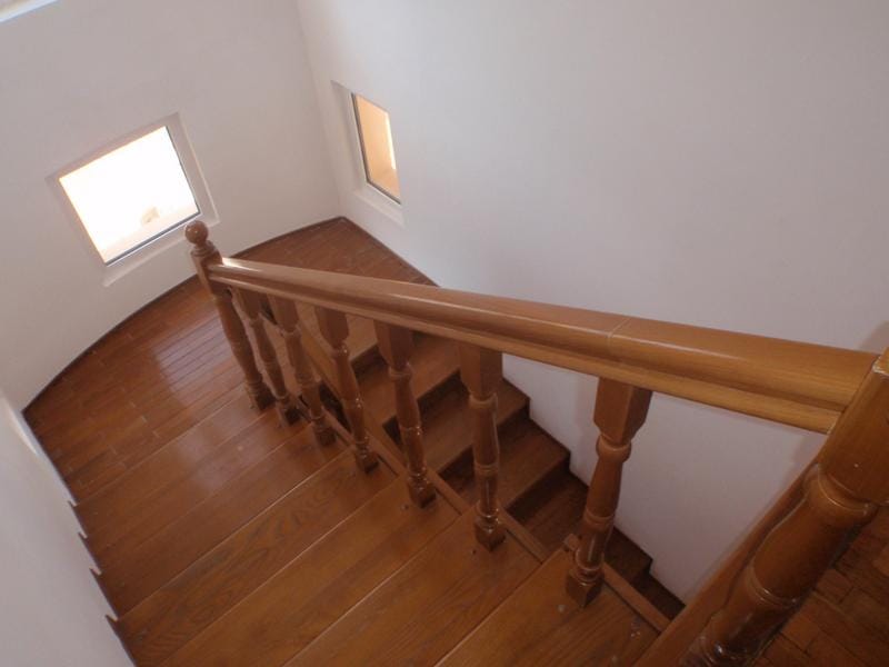 Wooden staircase with wooden railing and two small windows on a white wall.