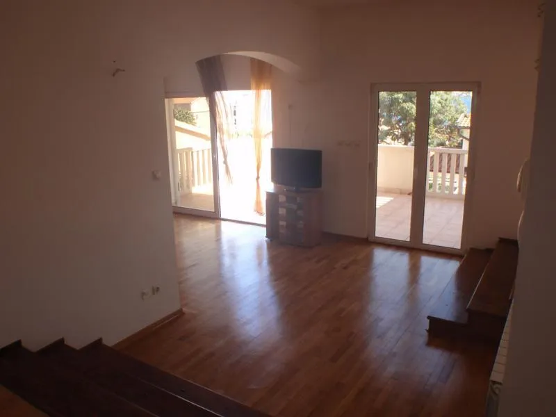 Empty room with wooden flooring, a TV on a stand, and glass doors leading to an outdoor balcony area.