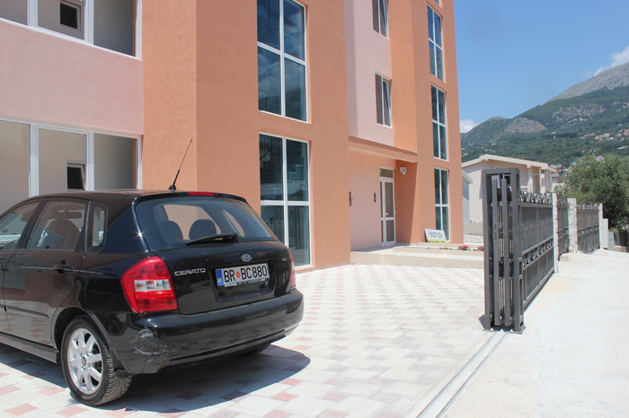Modern residential building with panoramic windows and parking in Dobra Voda, Montenegro. View of the building facade and mountains.