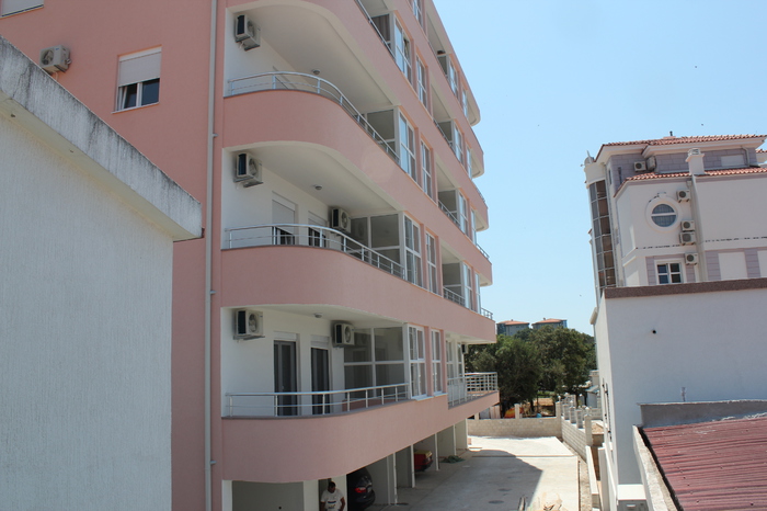 Facade of a modern residential building with balconies in Dobra Voda, Montenegro: view of the building and parking area near the house.