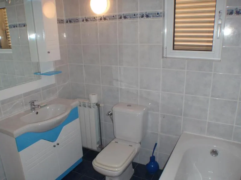 Bathroom featuring a sink, toilet, bathtub, grey wall tiles, and blue accents.