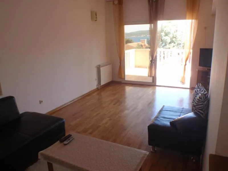 Living room with wooden floors, black sofa, coffee table, and glass doors leading to a balcony with sea view.