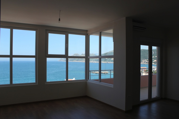Living room with panoramic windows and sea view in an apartment, Dobra Voda, Montenegro: bright finishes and access to the balcony.