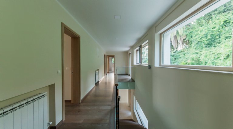 Bright corridor of a villa in Herceg Novi, Montenegro: wooden floor, panoramic windows overlooking the garden, and a staircase.
