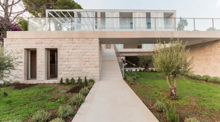 Exterior of a modern house featuring a stone wall, staircase, and green garden lawn.