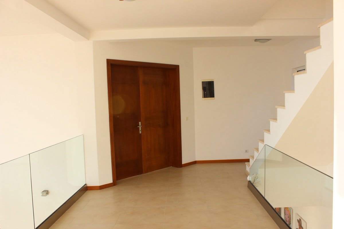 Interior of a house in Dobra Voda, Montenegro: a bright hall with a staircase, glass railings, and wooden doors.