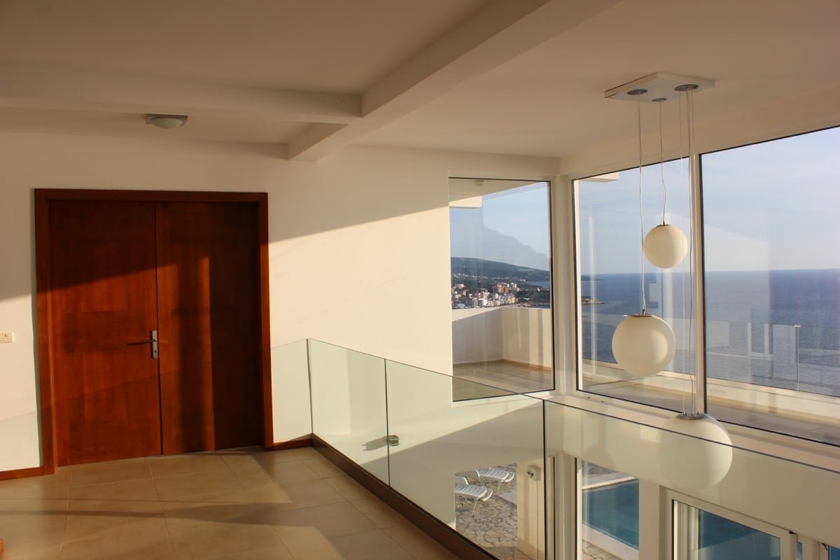Modern living room with panoramic windows and sea view in a house, Dobra Voda, Montenegro. Glass railings and terrace.