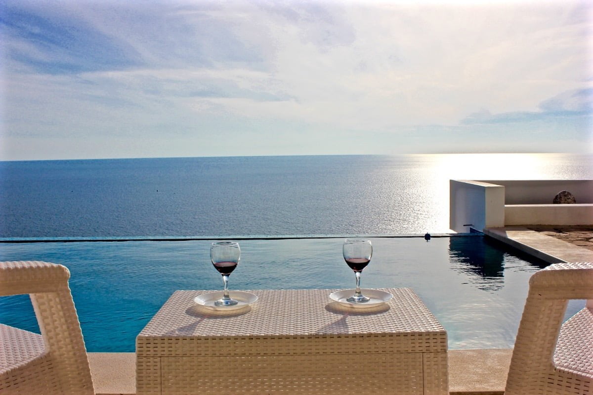 View of the infinity pool and the sea from the terrace of a house in Dobra Voda, Montenegro: wicker furniture and glasses of wine.