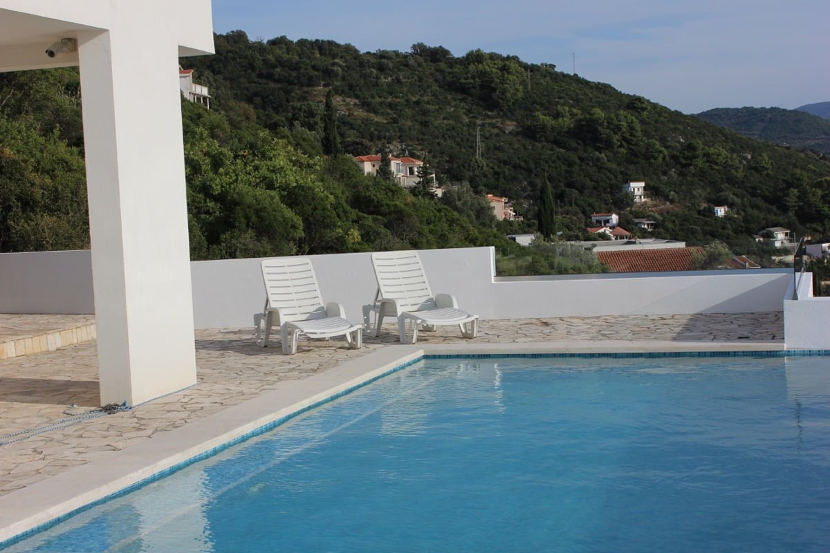 Pool by the house in Dobra Voda, Montenegro: terrace with sun loungers, stone finish, and panoramic mountain views.