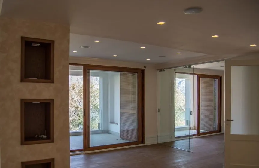 Empty room with wooden flooring, recessed wall niches, and large glass sliding doors leading outside.