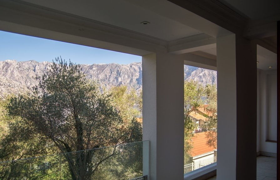View from the villa balcony in Stoliv, Montenegro: a panorama of mountains, olive trees, and tiled house roofs.