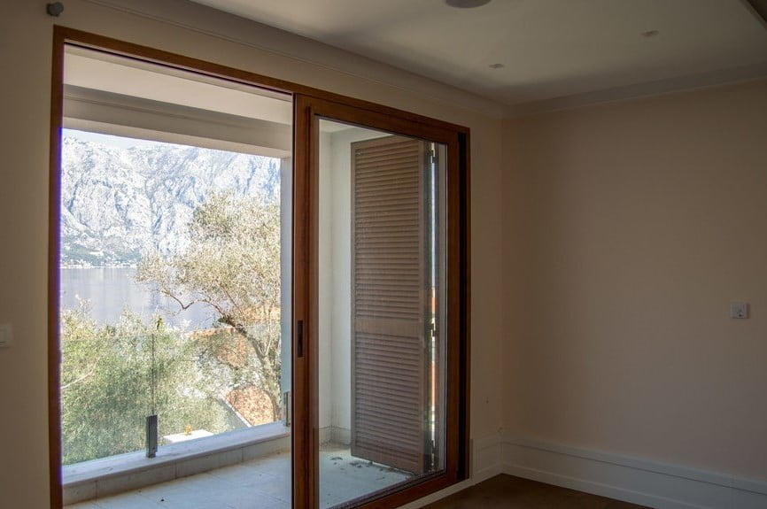 Empty room with wooden frame and sliding door leading to a balcony overlooking mountains and water.