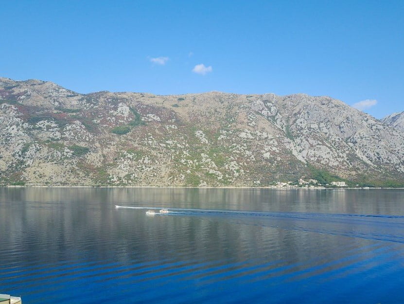 Panoramic view of the Bay of Kotor and the mountains from a villa in Stoliv, Montenegro, with boats passing on the water.
