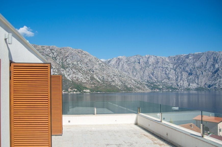 Villa terrace in Stoliv, Montenegro, with panoramic views of the Bay of Kotor and the mountains, glass railing, wooden shutters.