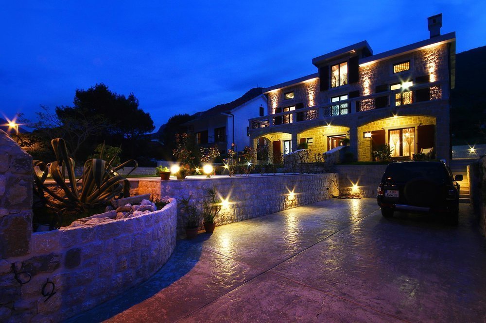 Two-story stone villa in Prčanj, Montenegro, with nighttime facade lighting, a terrace, and parking next to the house.