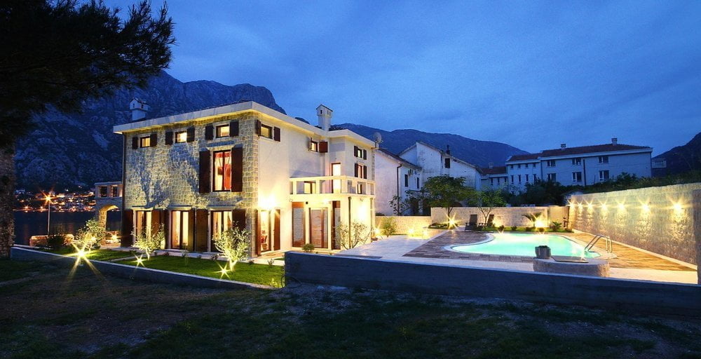 Two-story villa in Prčanj, Montenegro, with a swimming pool, stone facade finish, and evening lighting by the sea.
