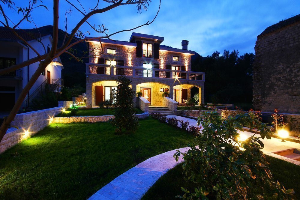 Two-story stone villa with lighting and a garden in Prčanj, Montenegro: front view in the evening.