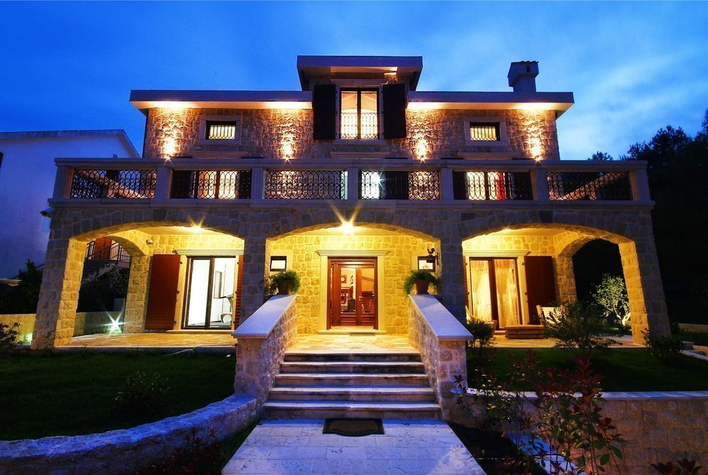 Three-story stone villa with lighting and a terrace in Prčanj, Montenegro: front view in the evening.