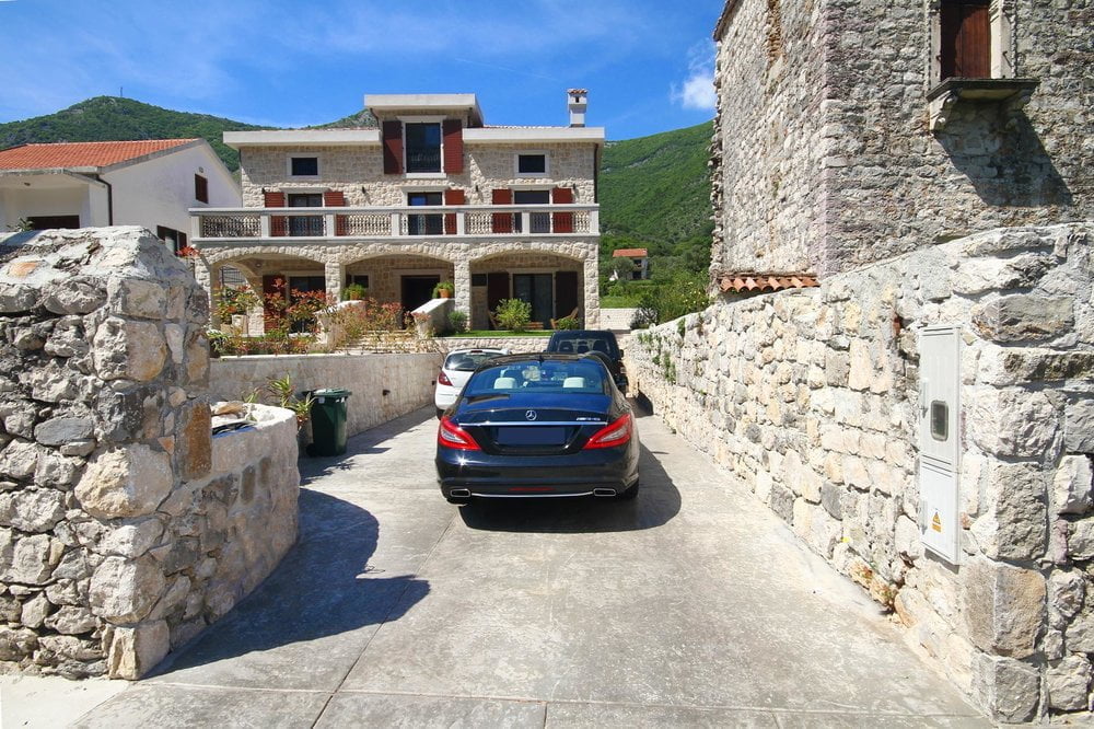 Stone villa in Prčanj, Montenegro: building facade, terrace, parking area with a car, and mountain view.