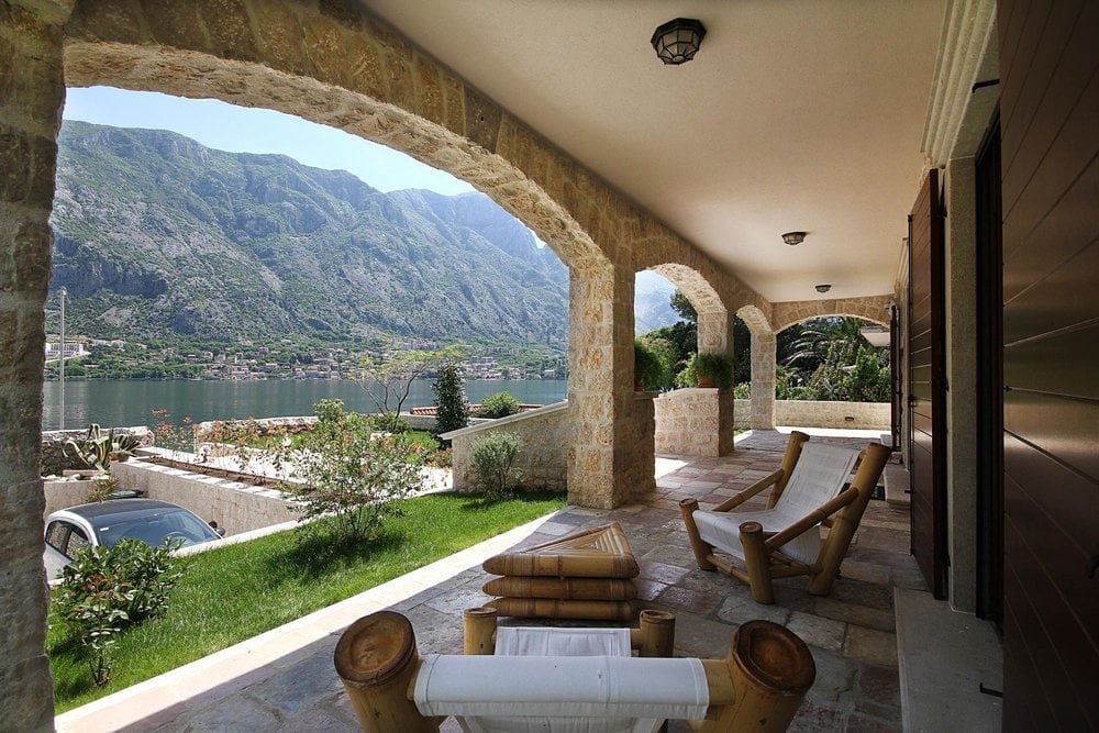 Stone terrace of a villa in Prčanj, Montenegro, with a view of the Bay of Kotor, mountains, and wicker furniture for relaxation.