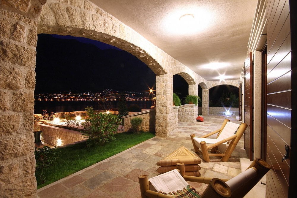 Villa terrace in Prčanj, Montenegro: stone arches, bamboo furniture, view of the night bay and garden.