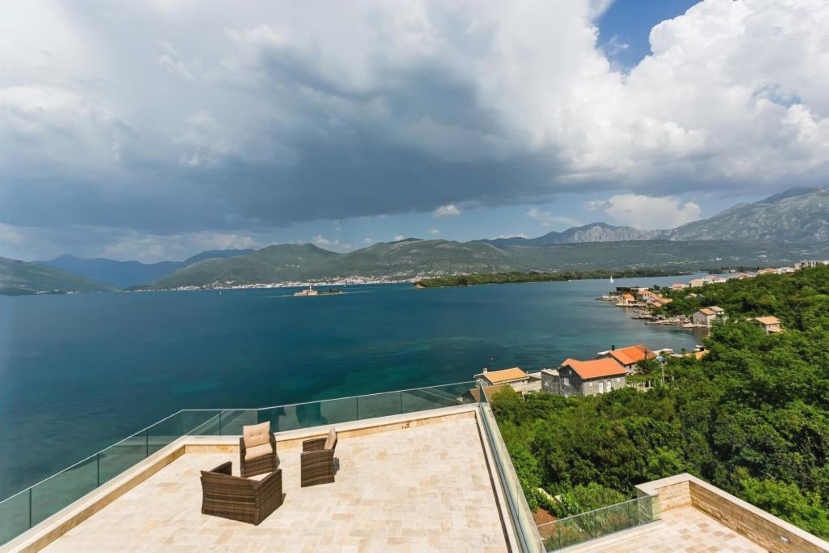 Terrace of a villa in Krašići, Montenegro, with panoramic views of the sea, mountains, and island, wicker chairs, and stone finishes.
