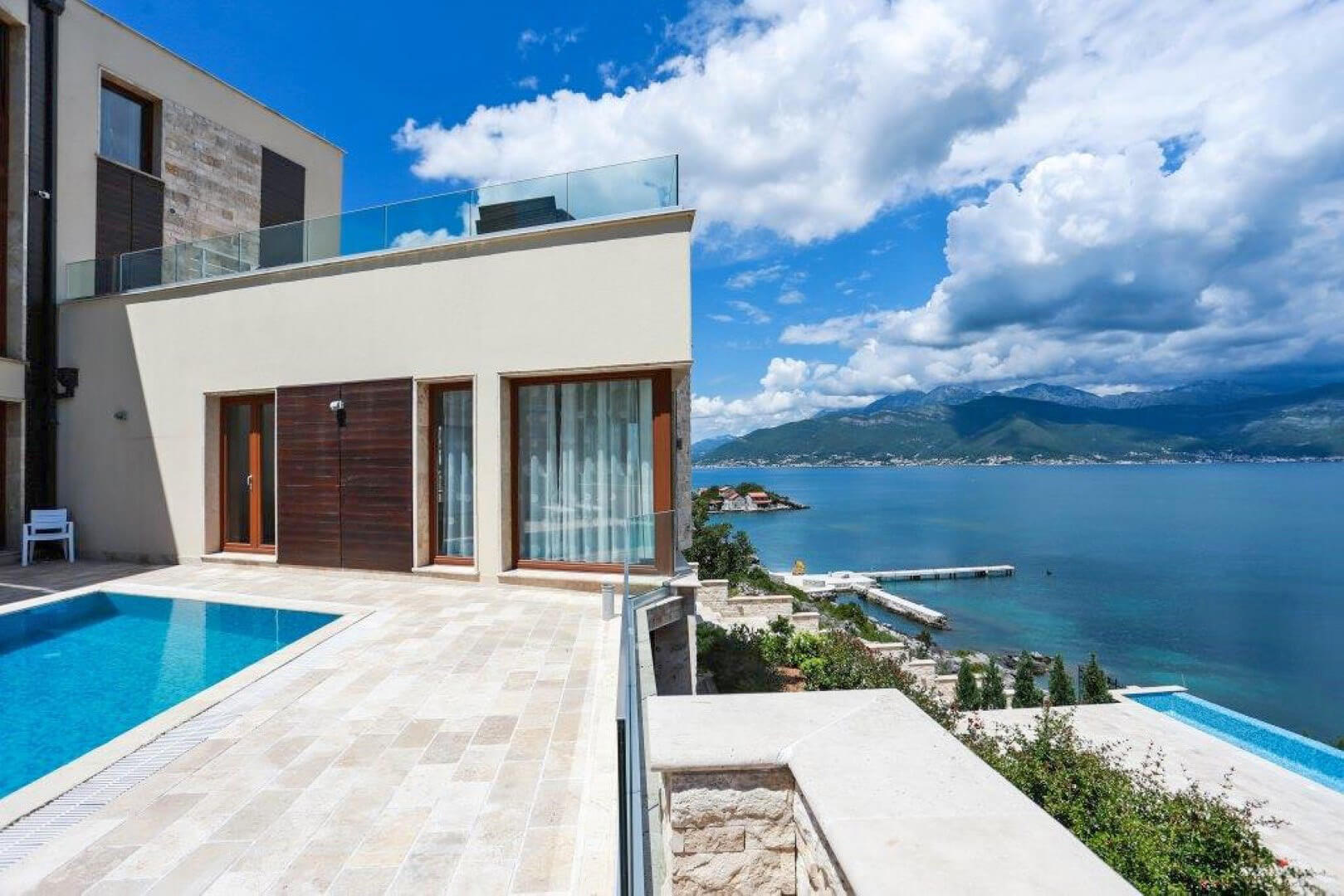 Modern villa with a pool and panoramic sea view in Krašići, Montenegro: terrace, stone finish, and mountains.