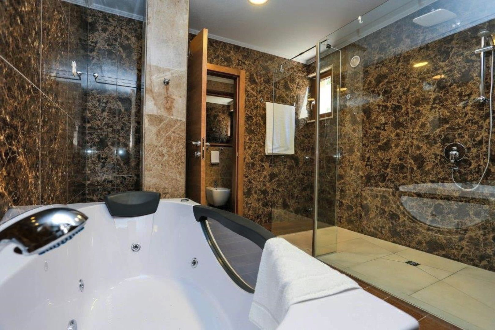 Bathroom with a jacuzzi and shower cabin in a villa in Krašići, Montenegro: walls finished with brown marble.