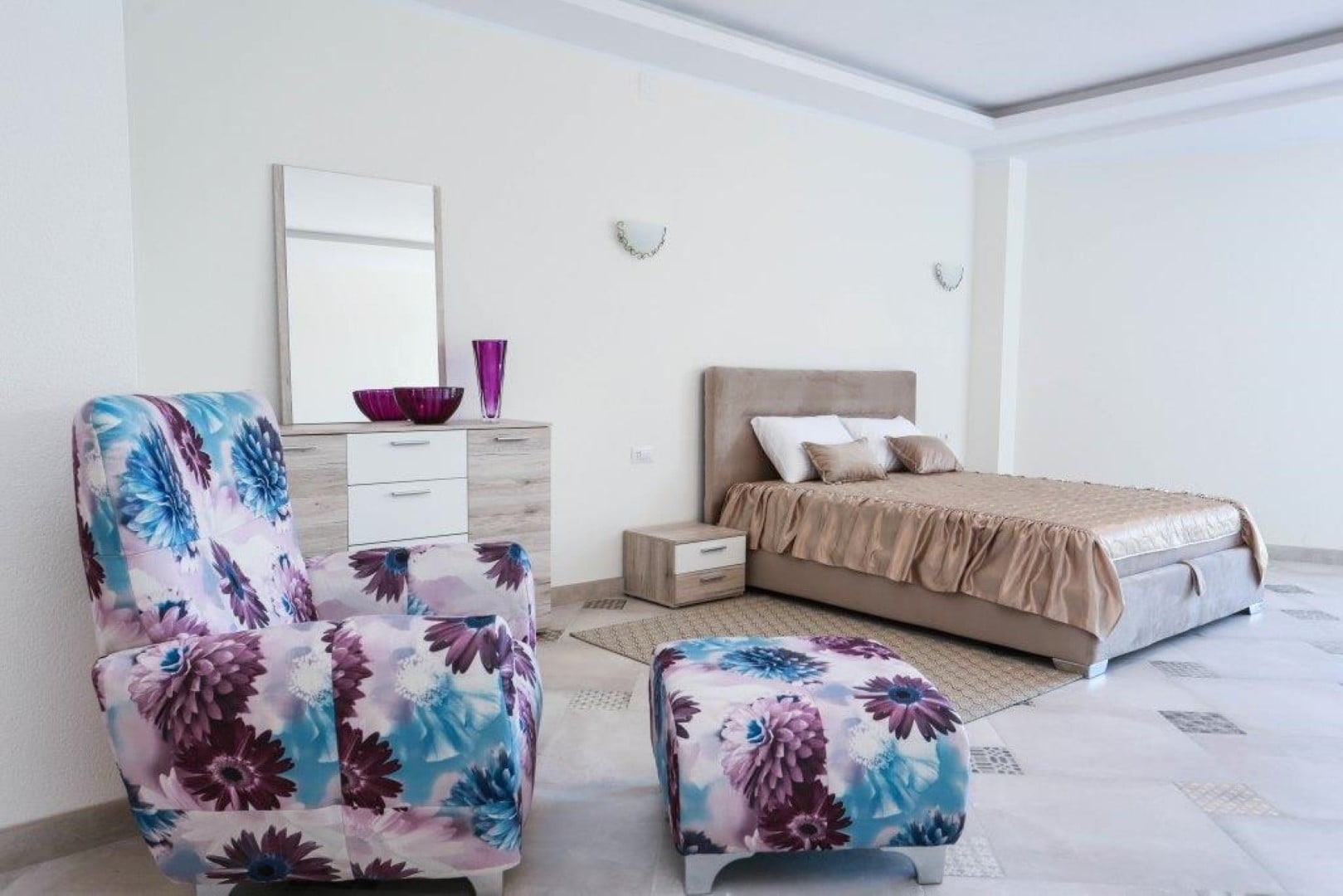 Bright bedroom in a villa in Krašići, Montenegro: a double bed, an armchair with a floral print, and a dresser with a mirror.