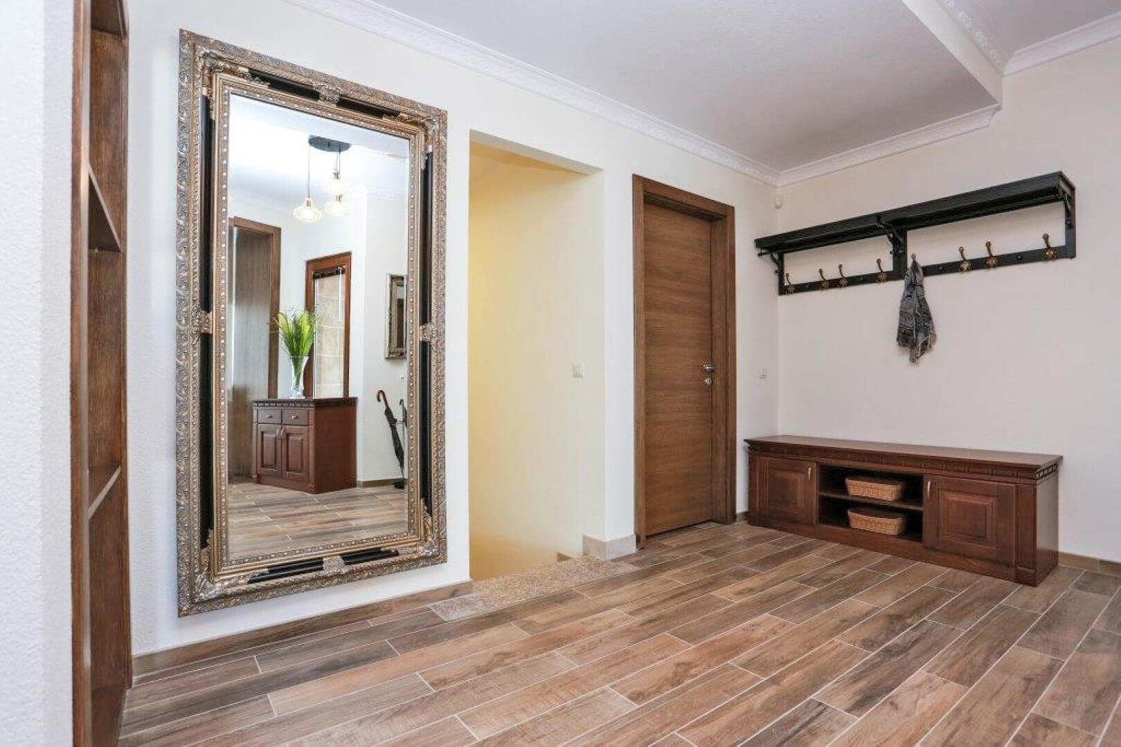 Villa hallway in Krašići, Montenegro: a large mirror in a gold frame, wooden furniture, and wood-look tiles.