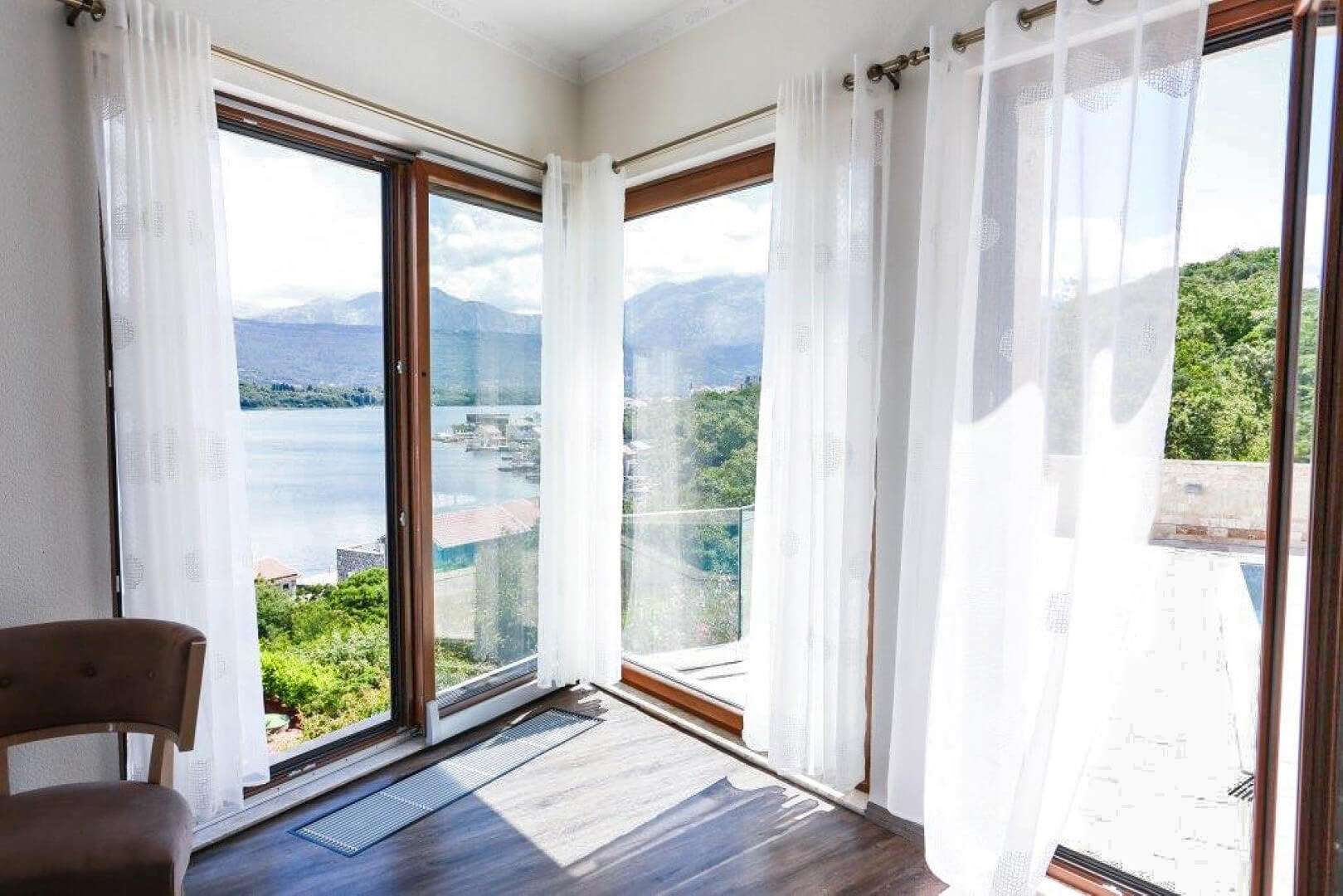 Living room with panoramic windows and a view of the sea and mountains in a villa, Krašići, Montenegro. Modern interior with a terrace.