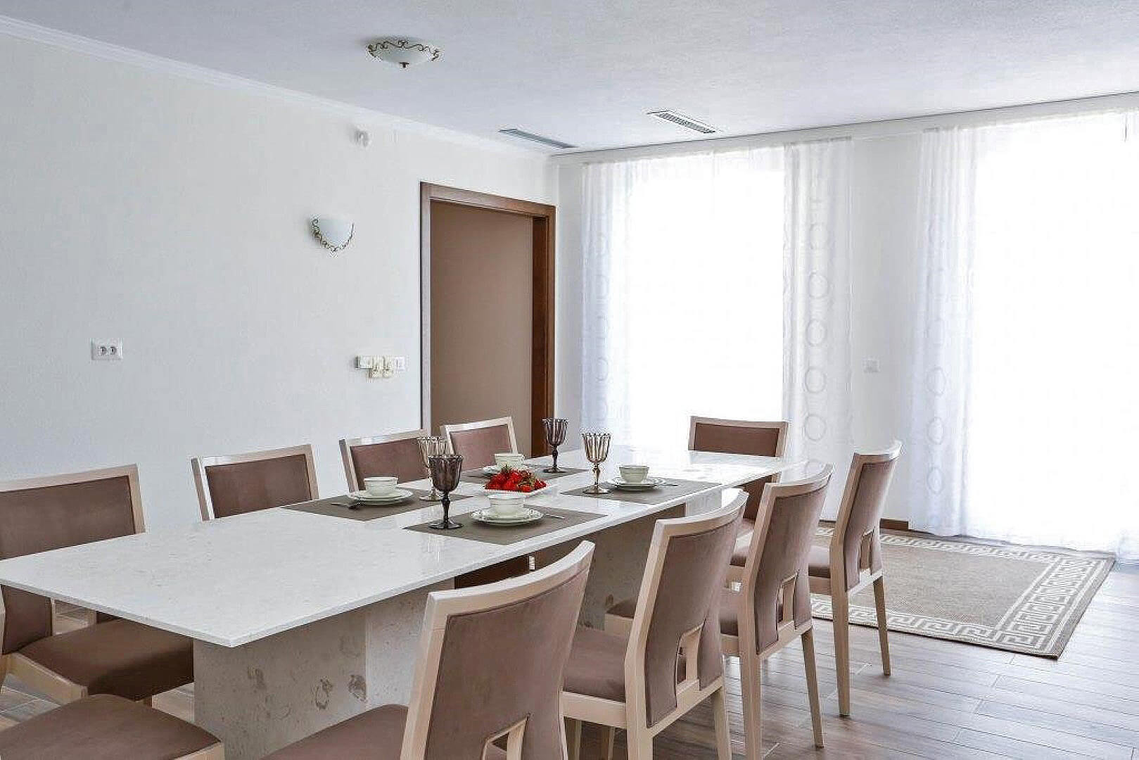 Bright living room with dining area in a villa in Krašići, Montenegro: large table, chairs, and panoramic windows.