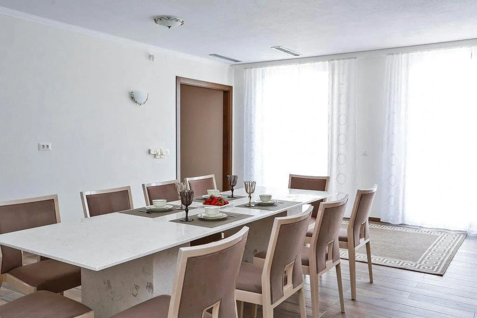 Bright room featuring a long white dining table surrounded by eight chairs set for a meal.