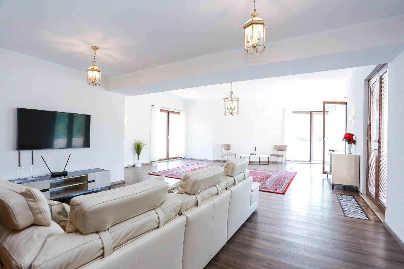 Bright living room with a white leather sofa and TV area in a villa in Krašići, Montenegro. Panoramic windows and parquet flooring.