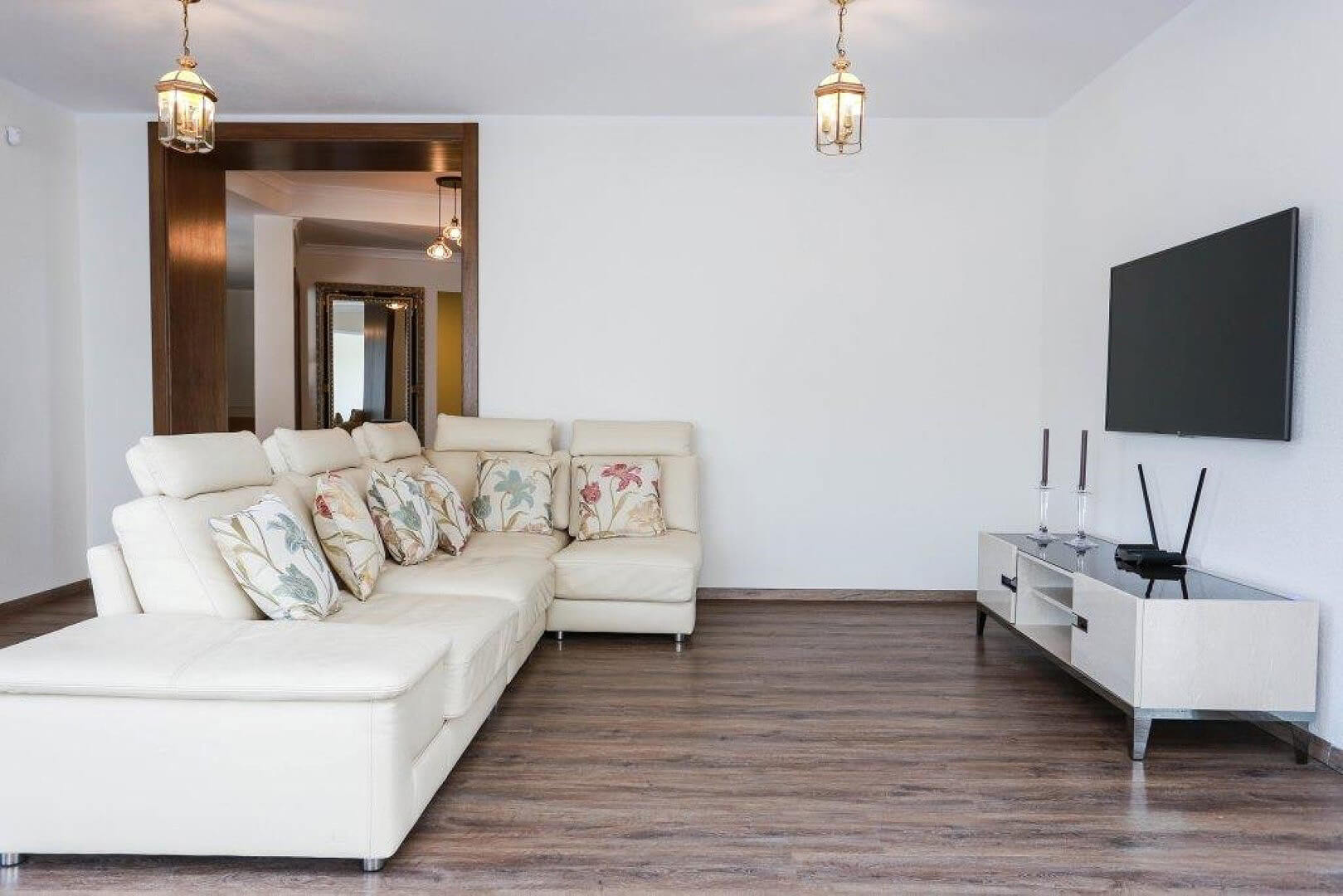 Bright living room with a white leather sofa and TV area in a villa in Krašići, Montenegro: modern interior with laminate flooring.