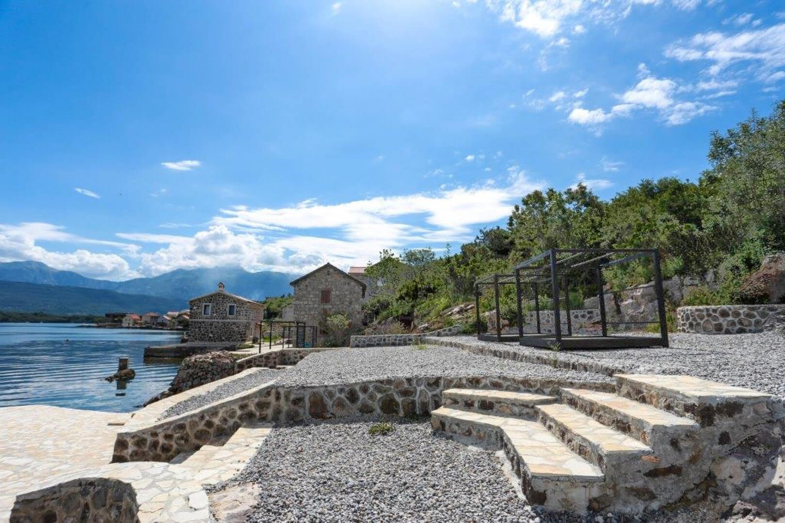 Villa terrace in Krašići, Montenegro: stone finish, lounge area with pergola, and panoramic view of the sea and mountains.