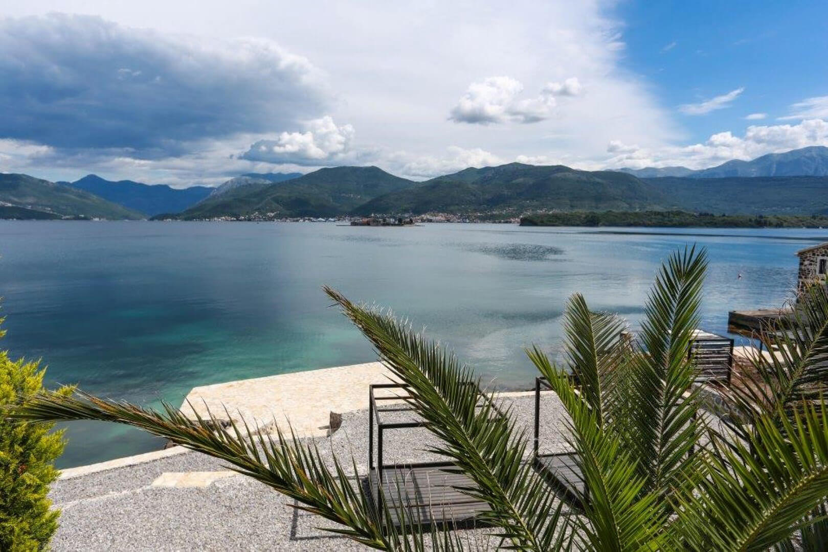 Panoramic view of the sea and mountains from the terrace of a villa in Krašići, Montenegro: private beach, palm trees, and a landscaped relaxation area.