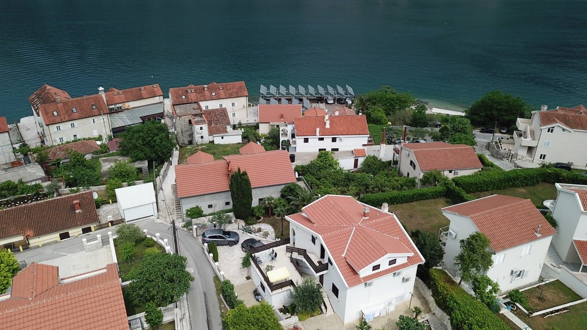 Aerial view of a villa in Prčanj, Montenegro: white houses with red tile roofs by the Bay of Kotor and a green area.