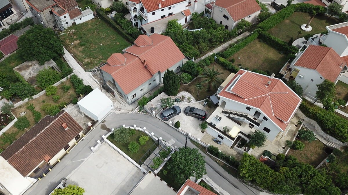 Aerial view of a villa in Prčanj, Montenegro: a private house with a tiled roof, parking, and a green plot.