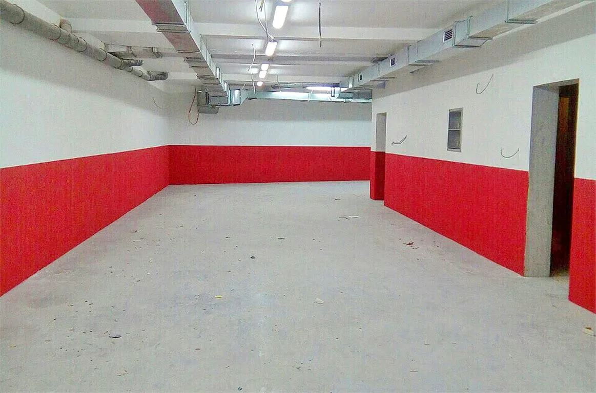 Empty room with red and white walls, exposed pipes and wiring on the ceiling, resembling a basement or storage area.