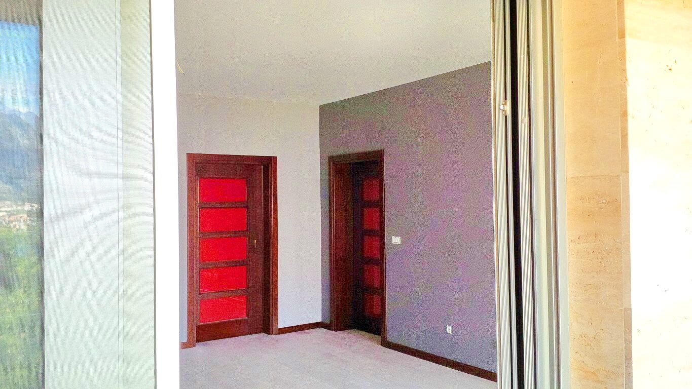 Living room interior in an apartment, Kotor, Montenegro: light walls, dark interior doors, and a view of the mountains from the window.